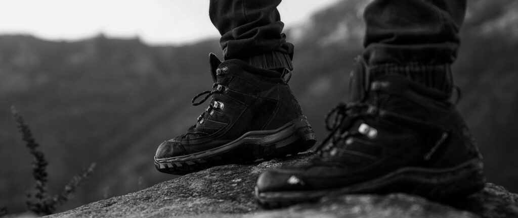 Close-up of hiking boots standing on a rock, showcasing outdoor adventure style in monochrome.