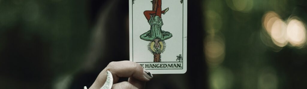 A hand holds the hanged man tarot card.