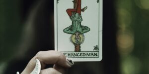 A hand holds the hanged man tarot card.