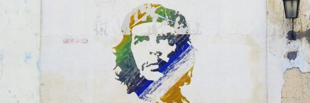 Colorful vintage cars parked by a mural on a Cuban street, showcasing local art and culture.