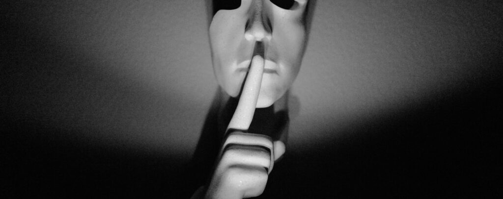 A white mask with a finger to its lips.