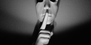 A white mask with a finger to its lips.