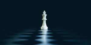 A single white chess king stands on a dark board.